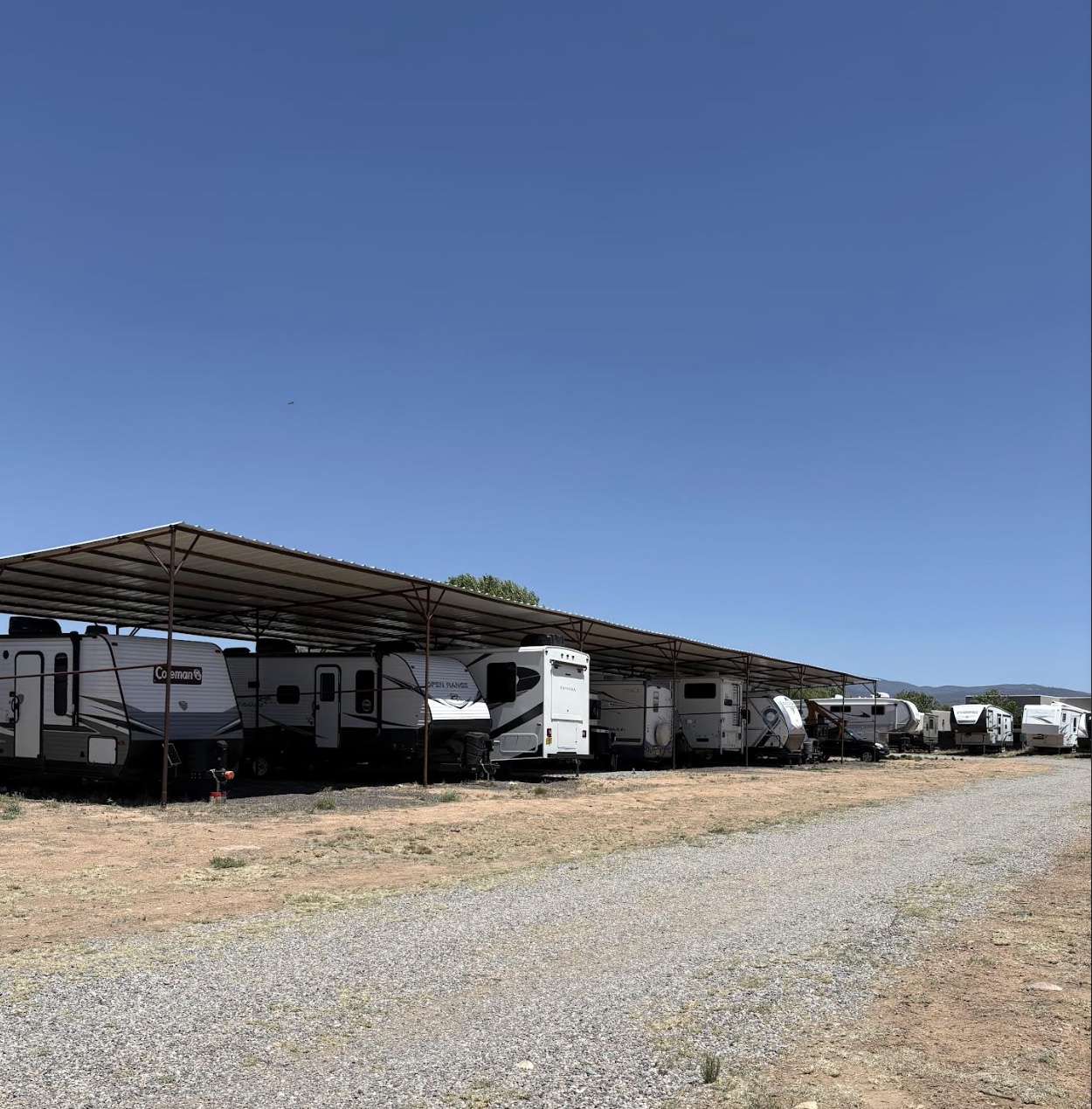 A long covered shade structure sheltering a row of RVs and travel trailers at the Santa Fe lot